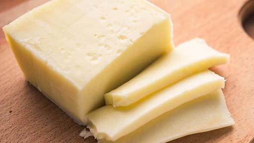 Block of cheese with several slices on a wooden cutting board.