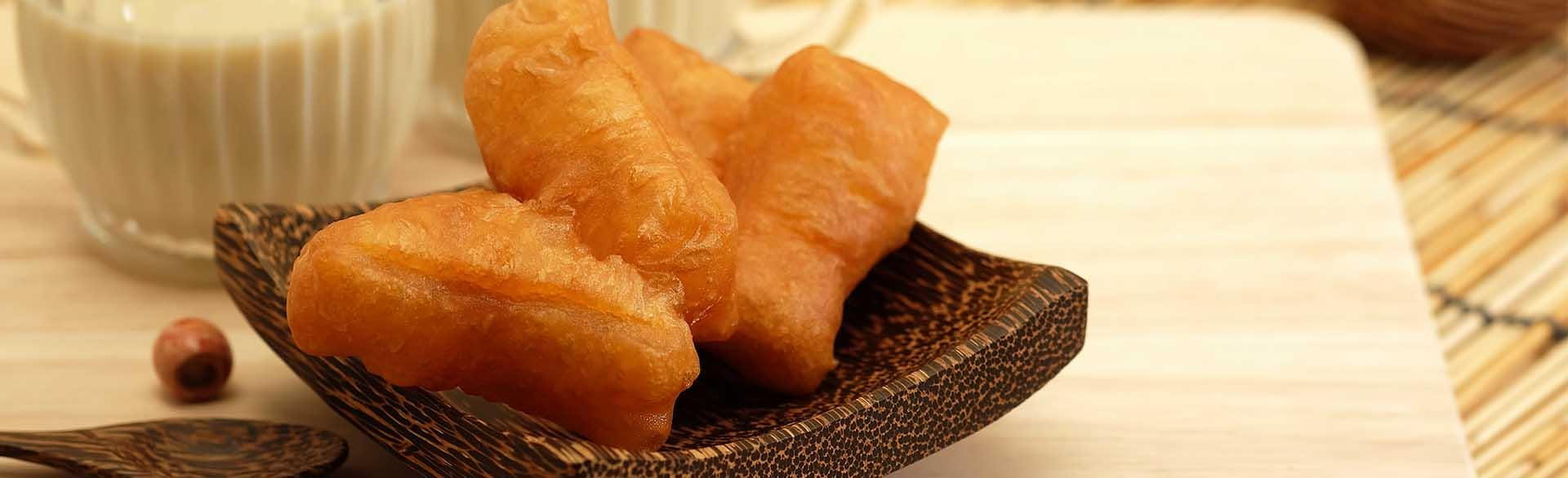 Wooden bowl with fried dough pieces, accompanied by glasses of milk and scattered nuts.