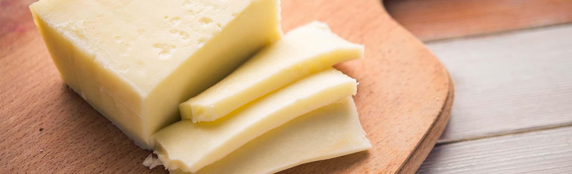 Block of cheese with several slices on a wooden cutting board.