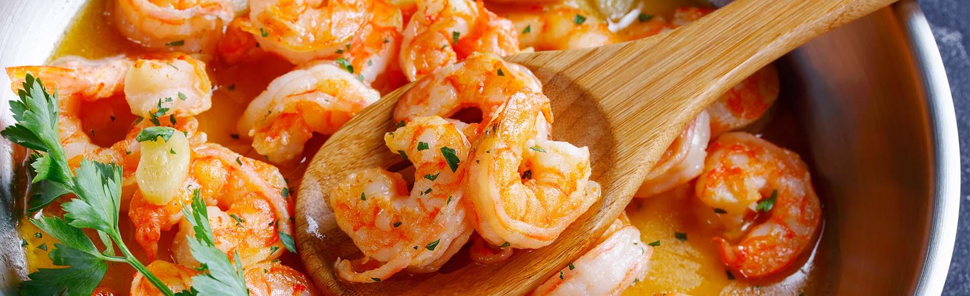 Cooked shrimp in sauce with herbs, scooped by a wooden spoon, and garnished with parsley.