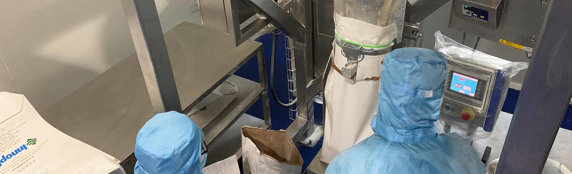 Two workers in blue suits handling materials and equipment in a processing facility.